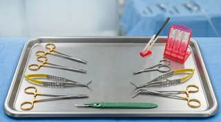 Surgical instruments on a stainless steel tray; needle holders, forceps, scissors, disposable scalpel, and Qlicksmart blade removers
