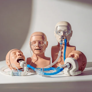 Adult airway management trainer head, pediatric intubation manikin, and difficult airway trainer with cricothyrotomy access on a simulation table.