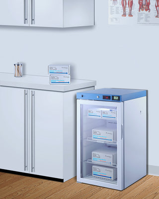 Medical refrigerator with labeled boxes inside, placed on a wooden floor in a clinical setting. Accucold ACR32GLHD 