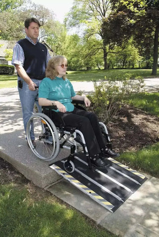Person using a wheelchair with a Clarke Healthcare MP210 DECPAC Portable Fiberglass Folding Wheelchair Ramp, assisted by another person, in an outdoor setting.