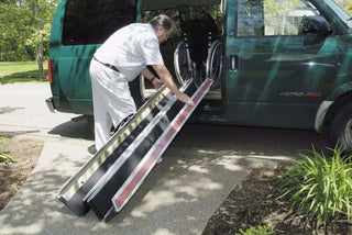 Person using a Clarke Healthcare MPEBXX DECPAC Fiberglass Portable Wheelchair Van Ramp with Edge Barrier to enter a green van.