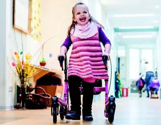 Child in a pink dress using a Clarke Healthcare Malte Posterior Size 0 to 4 Walker for Children in an indoor setting