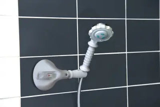 White Clarke Healthcare R1400202S Mobeli Shower Head Holder With Short Arm with flexible hose attached to a wall-mounted bracket on a black tiled wall.