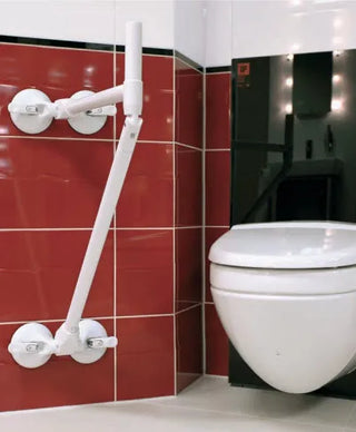 White toilet with a Clarke Healthcare R140026XSU Mobeli QuattroPower Support Angle Adjustable Grab Bar  against a red tiled wall in a bathroom.