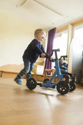 Child playing with a blue Clarke Healthcare S760XXXX Marcy Telescoping Rollator for Pediatrics indoors