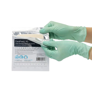 Person wearing green gloves holding a package Dynarex 3047 CuraFoam AG Silver Foam Dressings  on a white background