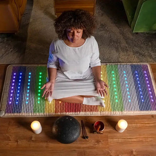 Woman meditating on a lit HealthyLine Rainbow Chakra mat between candles