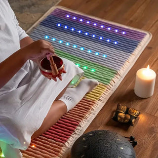 Person relaxing on a lit HealthyLine Rainbow Chakra mat near a candle