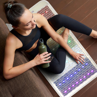 Woman sitting on a HealthyLine Rainbow Chakra mat with a water bottle