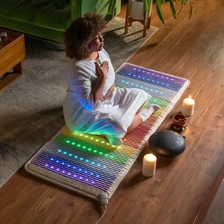 Woman sitting on a lit HealthyLine Rainbow Chakra mat