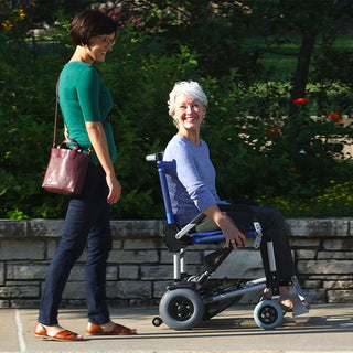 A woman riding the Journey Zinger 08300 power chair outdoors beside a friend on a garden path.