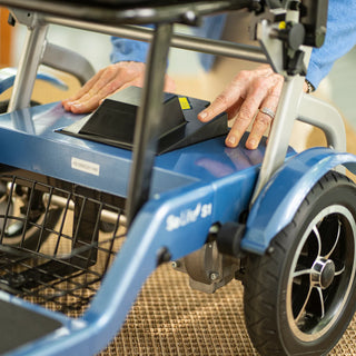 Hands releasing the removable battery on the frame of a blue Journey So Lite 08474 scooter.