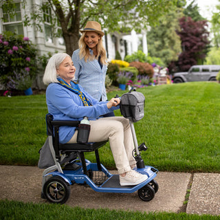 A woman on a Journey So Lite 08474 scooter on a pavement in front of a house with a lawn and flowers.