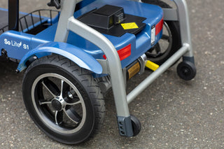 Close-up of the rear wheel, reflectors and anti-tipper wheels on a blue Journey So Lite 08474 scooter.