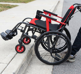 Close view of a Journey So Lite C2 08970 wheelchair being tipped over a kerb, front wheels up on the pavement and rear wheels still on the road.