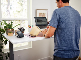 Man using a laptop at a Lifespanfitness TR5000BPro-SC130 Omni GlowUp Under Desk Treadmill with plants and decor in a home office setting