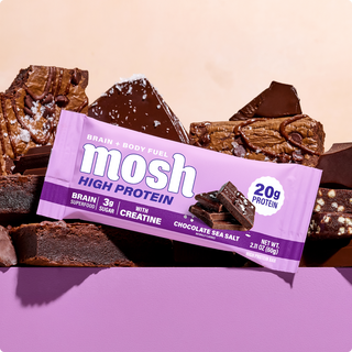 Wrapped MOSH Chocolate Sea Salt High Protein Bar resting on pieces of chocolate brownie