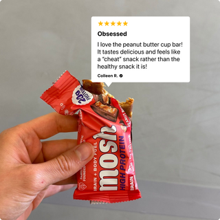 Hand holding an opened MOSH Peanut Butter Cup High Protein Bar beside a customer review