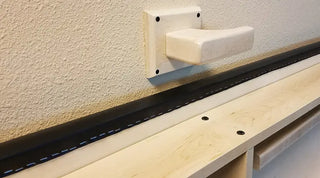 Pivotal Health Wall Mount Folding Treatment Table and white handle against a beige wall.