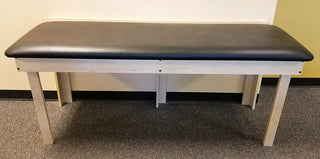 Pivotal Health Wall Mount Folding Treatment Table with a black top and white base in a room.