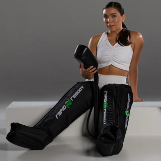 Woman kneeling in Rapid Reboot compression boots holding the REGEN control unit