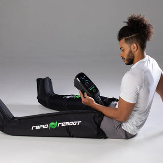 Man seated on the floor wearing Rapid Reboot compression boots and holding the REGEN control unit