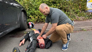 Person performing CPR on a person lying on the ground next to a car.