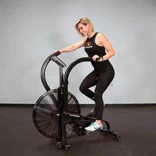 The Stroops AIRBIKE is a commercial fan exercise bike featuring a black steel frame, oversized front air resistance fan, moving upper-body handlebars, adjustable padded seat, foot pedals, and a wireless digital performance display mounted above the fan. Integrated transport wheels allow the bike to be moved easily while maintaining a heavy-duty commercial construction suitable for gyms, rehabilitation clinics, and performance training facilities.