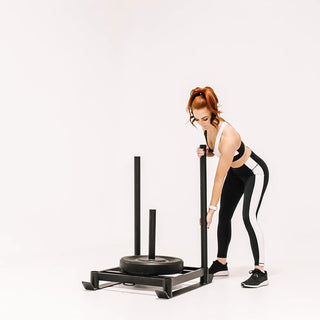 The Stroops BASE SLED is a rugged low-profile steel push sled with detachable upright push handles, a central base ring for adding weight plates, and steel rings on both sides for attaching a rope or battle rope for pushing and pulling exercises.