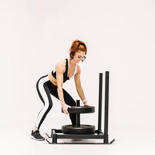 The Stroops BASE SLED is a rugged low-profile steel push sled with detachable upright push handles, a central base ring for adding weight plates, and steel rings on both sides for attaching a rope or battle rope for pushing and pulling exercises.