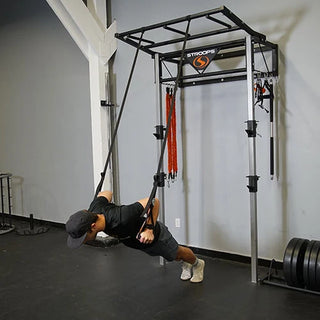The Stroops Body Weight Gym is a compact suspension training system featuring two textured grip handles with specialized loops and two long cloth straps for attaching to an overhead anchor point. The system is available with or without Slastix resistance bands.