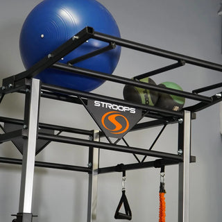The Stroops FSPR Performance Rack is a sleek, low-profile black fitness station with a sturdy rack structure, adjustable J-hooks for Olympic barbells, four resistance band anchor points, and upper storage space for workout equipment. The station is designed for resistance and power training and can accommodate up to two users.