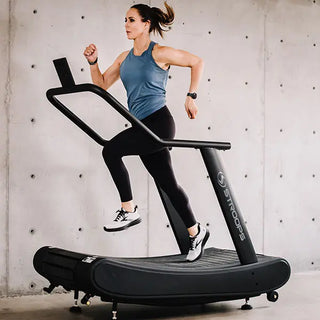 The Stroops OPTICURV is a commercial-grade curved motorless treadmill with a black steel frame and a curved, slat-style running surface. The treadmill features front support handles, a digital performance monitor, integrated transport wheels, and a self-powered design that allows users to control speed naturally without electricity, making it suitable for indoor running, sprint training, walking, and rehabilitation.