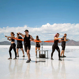 The Stroops REVOL Revolution Anchor is a circular black group fitness resistance system with six vertical pillars arranged around a central swiveling anchor structure. Multiple anchor points are positioned at different heights around the system for attaching resistance bands and supporting movement-based group training.