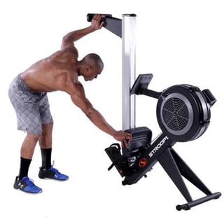 The Stroops SXR Xtreme Rower is a commercial rowing machine with a black flywheel housing, long aluminum monorail, ergonomic padded seat, adjustable footrests, and an angled padded handle. A user-friendly performance console is mounted above the flywheel, while integrated transport wheels and a foldable frame allow the rower to be moved and stored easily when not in use.