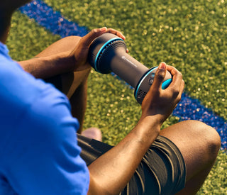 Seated athlete resting both palms on the Therabody CryoTherm Palm beside a pitch