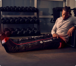 Athlete resting on the floor beside the Therabody JetBoots PRO Plus boots in a gym