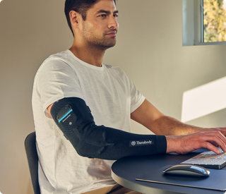 Man working at a desk while wearing the Therabody RecoveryPulse Arm sleeve