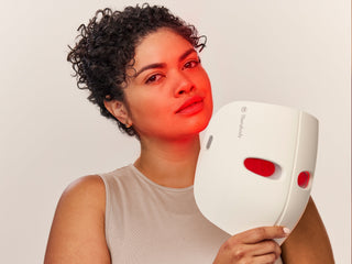 Woman holding the lit Therabody TheraFace Mask beside her face