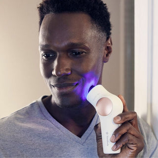 Man holding the Therabody TheraFace PRO against his cheek with the blue light ring lit