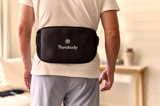 Person wearing a Therabody back wrap over the lower back in a living room