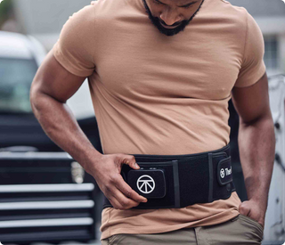 Man wearing the Therabody ThermBack LED wrap at the waist while standing outdoors