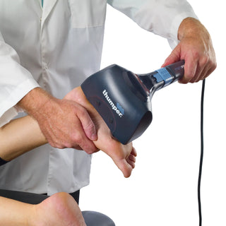 Thumper Mini Pro professional handheld percussion massager in dark gray and blue with an ergonomic long handle.