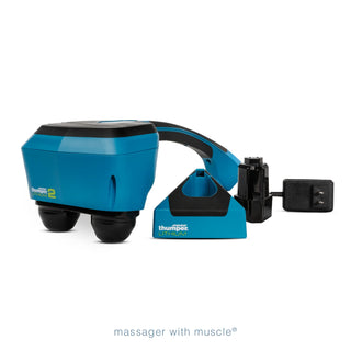 Thumper Lithium2 cordless percussion massager in black and teal with rechargeable battery and charging nest.