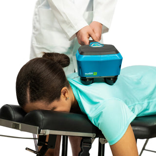 Thumper Lithium2 cordless percussion massager in black and teal with rechargeable battery and charging nest.