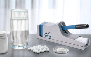Viva Comfort ADIME950-01 pill crusher on a table beside a water glass, white tablets and powder