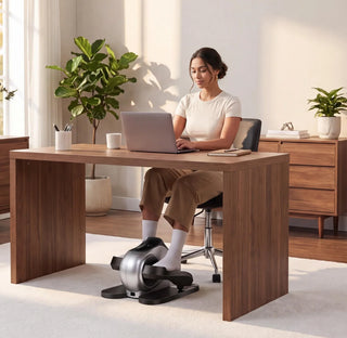 Woman working at a desk while using the WalkingPad E1 elliptical underneath