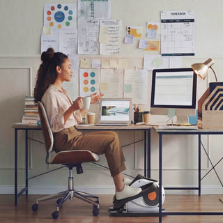 Woman at an office desk using the WalkingPad E1 elliptical under her chair