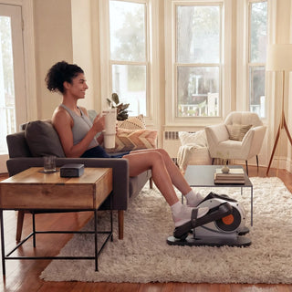 Woman using the WalkingPad E1 elliptical while sitting on a sofa