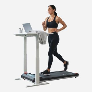 Woman jogging on the WalkingPad Massage Step treadmill beside a standing desk